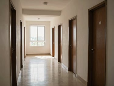 Wide interior corridor of a mid-rise apartment building in Chennai, natural north light flooding through end window, polished floor tiles, numbered apartment doors in a row