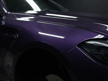 Sleek automotive photography of a freshly painted deep purple car fender reflecting soft studio light, high-contrast specular highlights, 50mm lens