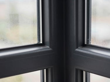 Macro architectural detail shot of a flush corner joint on a matte black window frame, crisp natural overcast light highlighting the textured finish