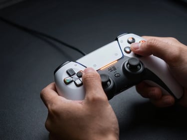 Hands gripping a game controller in low-key side-light, reflective chrome triggers catching a narrow amber beam, deep shadow on matte black background, extreme close-up framing isolating fingers and hardware detail
