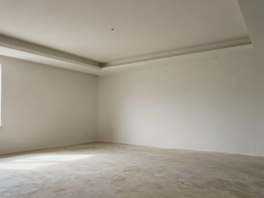 Wide shot of a completed living room with a flush false ceiling featuring recessed lighting, mid-morning diffused natural light, neutral plaster finish, empty room showing ceiling-to-floor proportion and spatial integration, no people