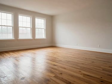 Wide environmental shot of a freshly cleaned living room after completion: hardwood floors polished, baseboards bright, surfaces clear — natural daylight from side windows, sharp and unfiltered, no staging or props