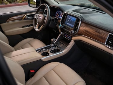Overhead close-up of a GMC Yukon Denali interior — stitched leather seats, illuminated instrument cluster, premium trim detail, soft ambient cabin lighting, editorial product photography