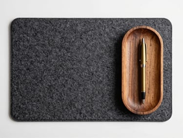 Top-down view of a dark grey felt desk mat with a wooden tray holding a brass pen, clean minimalist setup