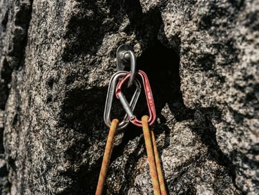 Extreme close-up of technical climbing rope and carabiners on a sheer granite wall, dramatic high-contrast alpine light, desaturated tones.