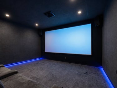 Wide architectural shot of a dark, luxurious home theater room, charcoal acoustic panels, glowing blue LED floor trim, massive projection screen.