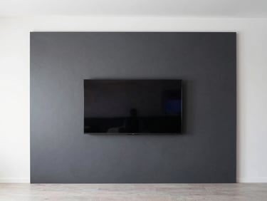 Wide shot of a minimalist living room, a perfectly flush-mounted flat screen TV on a charcoal accent wall, zero visible wires.