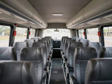 Interior shot of a Monif Transport long-distance coach showing rows of clean upholstered seats, safety belts visible on each seat, overhead luggage rails, natural light from side windows illuminating the aisle, no passengers