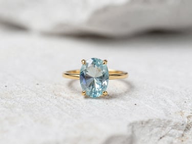 Close-up of a custom gold ring featuring a raw aquamarine gemstone, soft natural mountain daylight, clean white stone backdrop, macro lens.