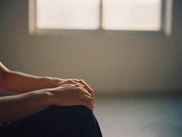Close-up of hands resting on knees in a quiet, minimalist studio space, soft-focus, warm golden-hour daylight, 35mm film.