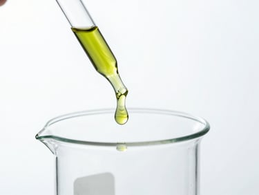 Amber oil dropping from a glass pipette into a clean laboratory beaker, sterile high-contrast white background, cool daylight