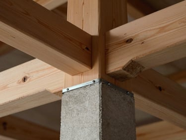 Extreme close-up of heavy timber joinery meeting a poured-in-place concrete pillar, showing the clean structural lines and technical steel connection plate.