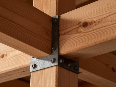 Extreme close-up of heavy timber joinery, a thick cedar beam meeting a dark steel connection plate with heavy bolts, warm side lighting highlighting wood grain and metal texture