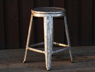 Traditional rustic cowboy stool made of cast aluminum, outdoor farm setting, sunset side light highlighting the sturdy legs.