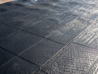 Close-up of high-performance black HDPE geomembrane texture showing the textured grip surface, natural bright daylight highlighting the precise engineering pattern, clean industrial aesthetic.