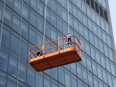 Rope suspended platform hanging against a clean modern glass skyscraper facade, bright daylight