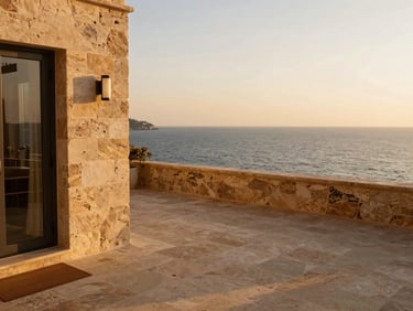 Boutique hotel terrace overlooking the sea at golden hour, warm stone textures, soft natural light