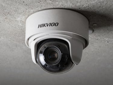 Close-up of a Hikvision PTZ dome camera mounted on a concrete ceiling bracket, steel housing detail visible, cool studio strobe lighting, no people
