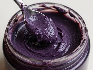 Close-up of a rich purple hair mask being scooped from a dark glass jar, thick creamy texture visible, marble surface, north-facing daylight, no text