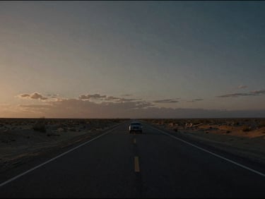 Wide cinematic 35mm film still, extreme wide shot of a lone car on an endless desert highway under a bruised twilight sky, dramatic low-key lighting.