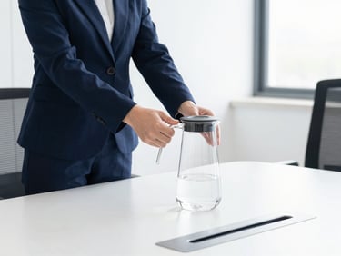 A uniformed specialist placing a pristine glass water carafe on a modern minimalist office conference table, bright daylight