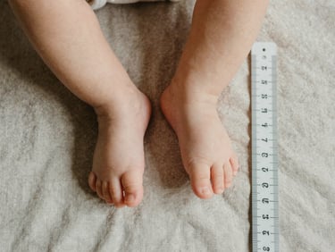 Overhead shot of a small infant foot next to a ruler on a neutral linen surface, soft diffused window light, minimal and precise framing