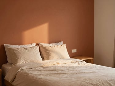 Cozy double room interior with warm terracotta accent wall, stone beige sheets, soft ambient light, minimalist wood furniture