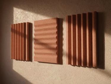 Warm architectural photography of modular acoustic boards mounted on a textured plaster wall, soft directional afternoon sunlight casting long shadows, muted terracotta tones, medium format film.