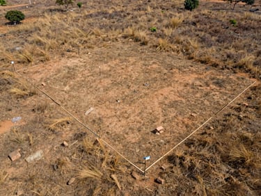 Overhead shot of a surveyed land plot in Lagos outskirts, boundary markers visible, dry savanna grass at edges, even daylight, no people