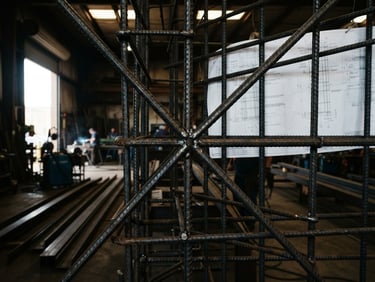 Close-up of structural rebar cage, precisely welded, with architectural blueprints overlaid, high-contrast workshop light, deep metallic tones, sharp focus on steel textures, 35mm.