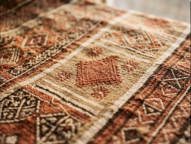 A close-up of a traditional hand-woven Sahelian textile with intricate terracotta and sand geometric patterns, warm natural window lighting, rich earth tones.