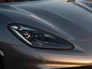 Sleek detail of a luxury superesportivo car headlight, dark metallic paint reflecting golden Rio sunset, high-contrast shadows.