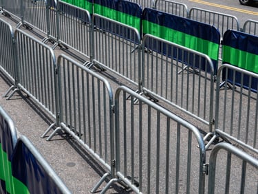 Neat rows of metal barricades structuring a public street parade route under bright daylight, orderly layout