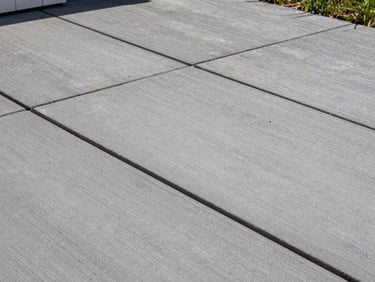 Overhead close detail of newly laid concrete pavers on a finished residential patio, natural daylight, tight grout lines, clean flush surface, slate-gray tone, no people