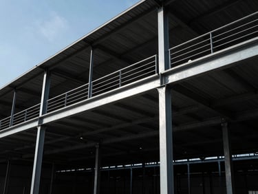 Industrial mezzanine structure with steel beams, showing an upper level for storage or offices, wide-angle shot, high-contrast industrial daylight.
