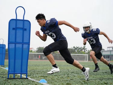 High-action youth football training in Enoch, a player mid-sprint past blue training cones, sharp action freeze, high-contrast overcast daylight.