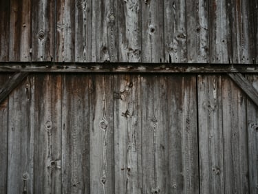 Close-up of weathered historic barn siding showing original scribe marks, low-contrast natural overcast daylight, desaturated earth tones