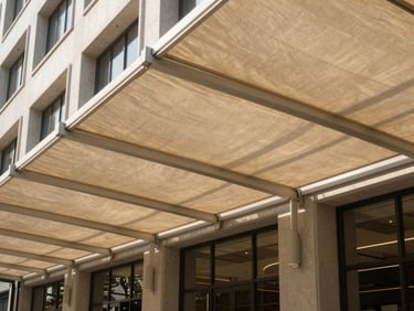 Wide environmental shot of a contemporary architectural awning canopy fixed to the facade of a commercial building, taut woven fabric panels blocking low afternoon sun, natural daylight, no people, clean geometric shadow lines