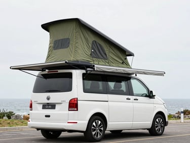 Three-quarter rear view of a white high-roof campervan at a coastal car park, pop-top raised, bespoke olive-green awning extended from the side, sky overcast and bright