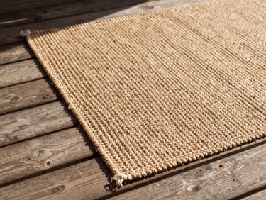 Overhead flat-lay of a textured jute rug corner on a weathered wooden patio deck, warm natural sunlight, 35mm.