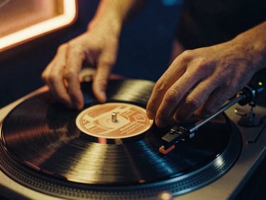 Close-up of hands gently placing a vinyl record needle onto a rotating turntable, warm gold light reflecting off the vinyl grooves, 35mm film grain