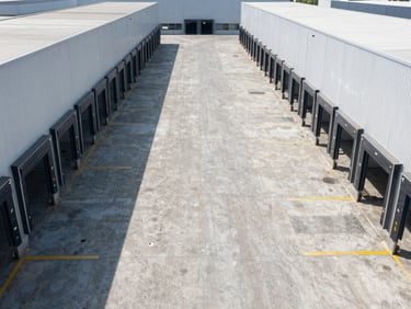 High-angle exterior shot of a modern distribution center, clean concrete pavement, symmetrical loading docks, cool daylight.
