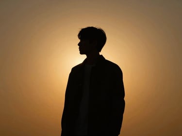 Dramatic high-contrast silhouette of a person standing against a warm glowing amber background, cinematic lighting