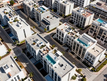 Aerial wide shot of a modern residential development in Valencia, clean geometric rooftops and pool terraces visible from above, bright midday light, sharp shadows, no people, DJI Mini 5 Pro perspective