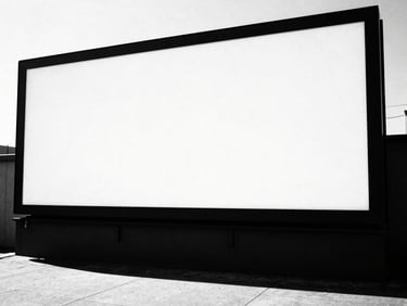 Wide environmental shot of a large-scale outdoor advertising billboard in an urban setting, bathed in harsh direct sunlight, casting a long, sharp shadow. High-contrast black and white photography, sharp focus, 35mm film grain.
