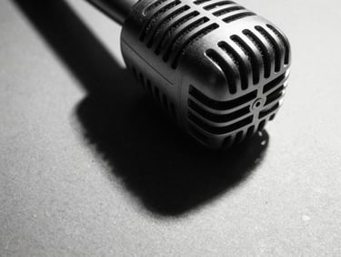 Extreme close-up of a vintage microphone with sharp, dramatic shadows on a textured surface, harsh studio light. High-contrast black and white photography, sharp focus, 35mm film grain.