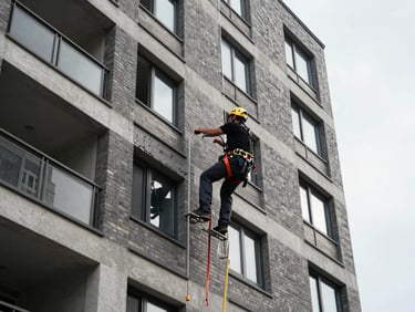Exterior view of a multi-story residential condominium facade, technician in full safety harness working on upper floor cladding, overcast natural daylight