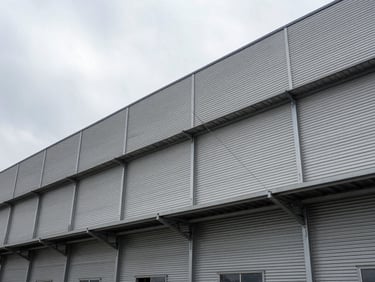 Wide-angle exterior of an industrial facility building facade under overcast light, metal cladding panels and structural elements visible, no people, technical environmental framing