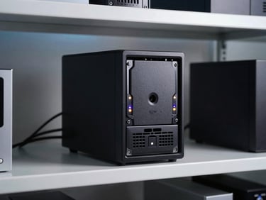 Synology NAS unit with drive bays visible and LEDs active, sitting on a shelf in a tidy home lab environment, cool studio lighting, cables managed with clips along the back panel
