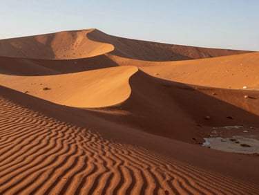Dramatic golden hour light casting long shadows over massive red sand dunes in the Namib desert, empty landscape.